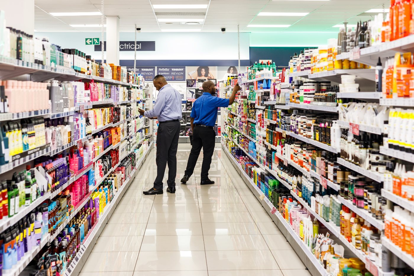 Retail merchandisers restocking health and beauty shelves in a South African store aisle